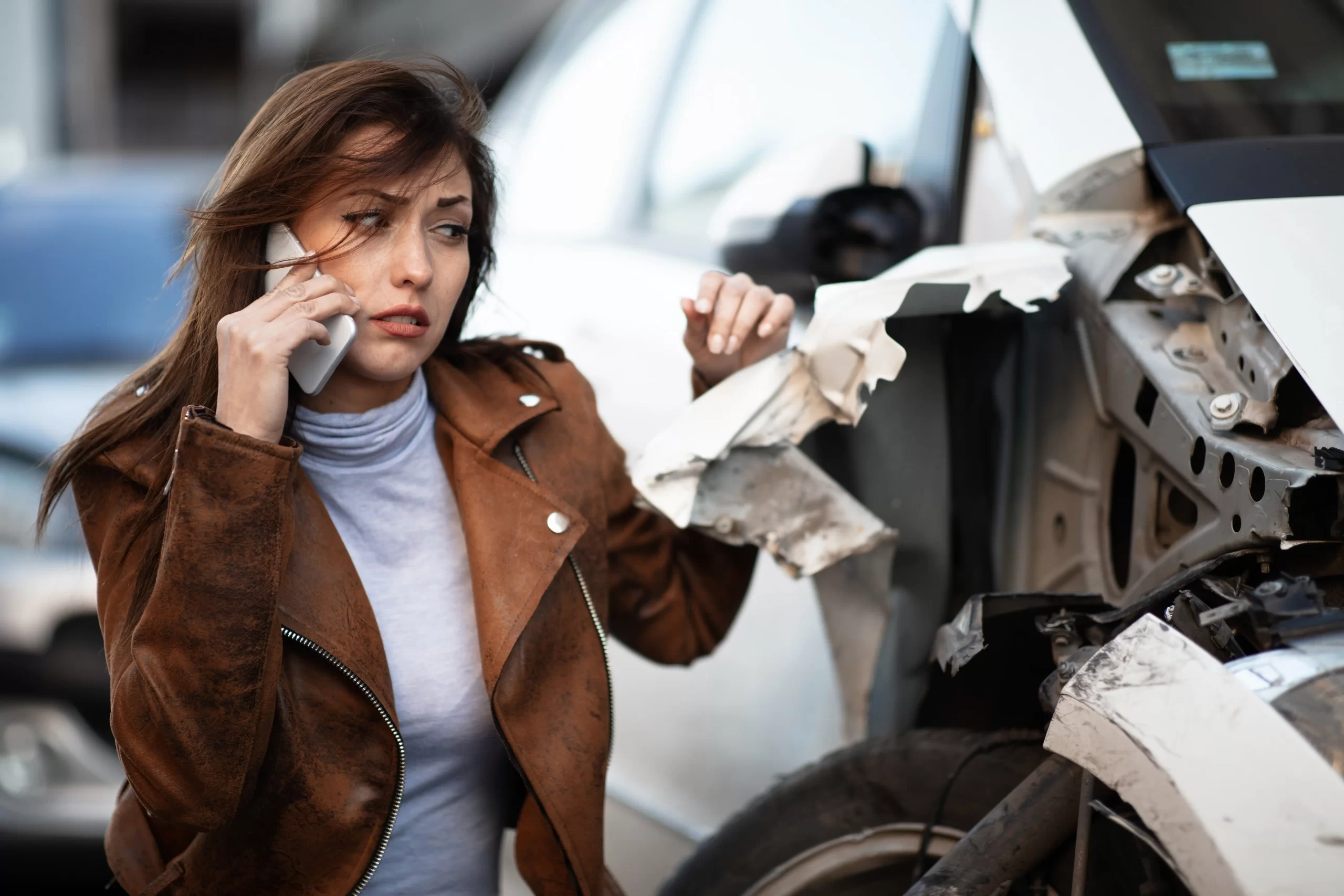 young sad woman using mobile phone calling help while looking her wrecked car scaled