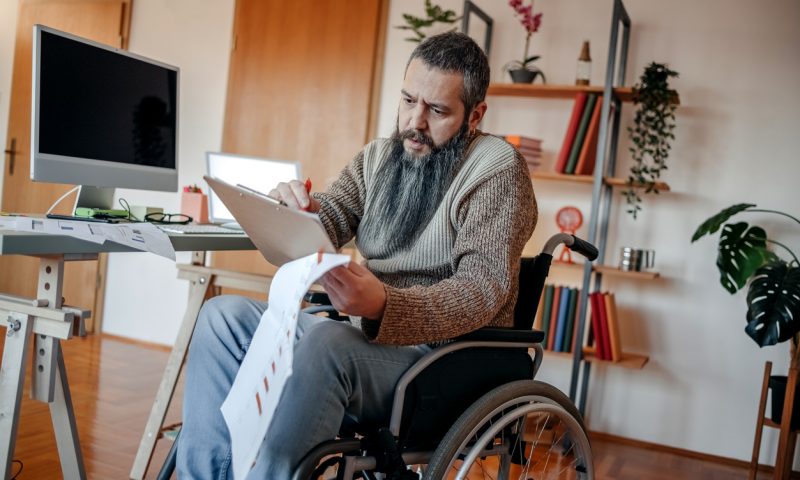 Person with disability working home office using using desktop PC and analysing results using charts