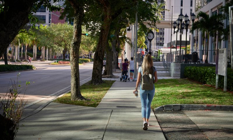 Female with backpack walking on empty sidewalk afternoon light back view