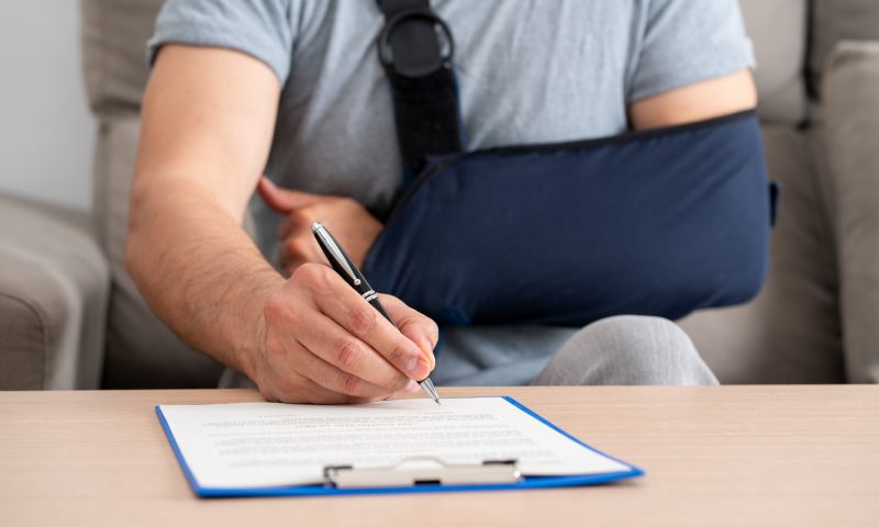 Front view of a handicapped man with sling signing contract at home