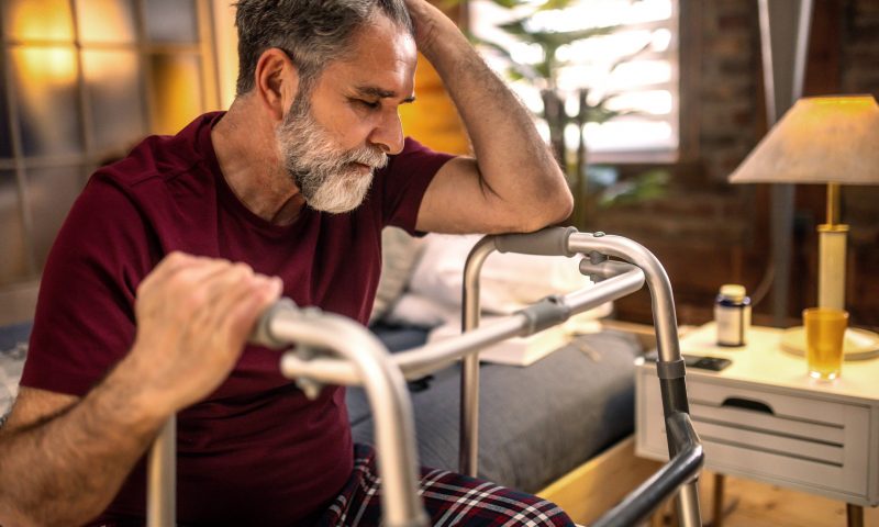 Thoughtful elderly man sitting alone at home with his walking cane