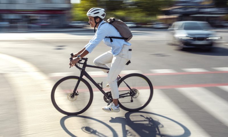 Multiracial female commuting to work with bicycle in an urban setting featuring motion and energy wearing a white helmet and casual business attire showing focus and determination.